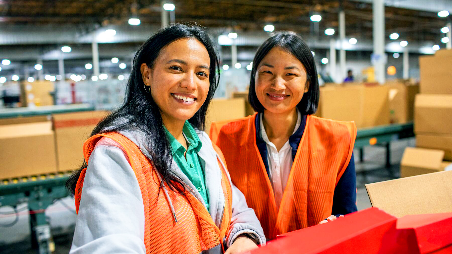 Two women smiling in a warehouse in orange vests
