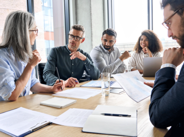 People sitting around a large table in an office People sitting around a large table in an office