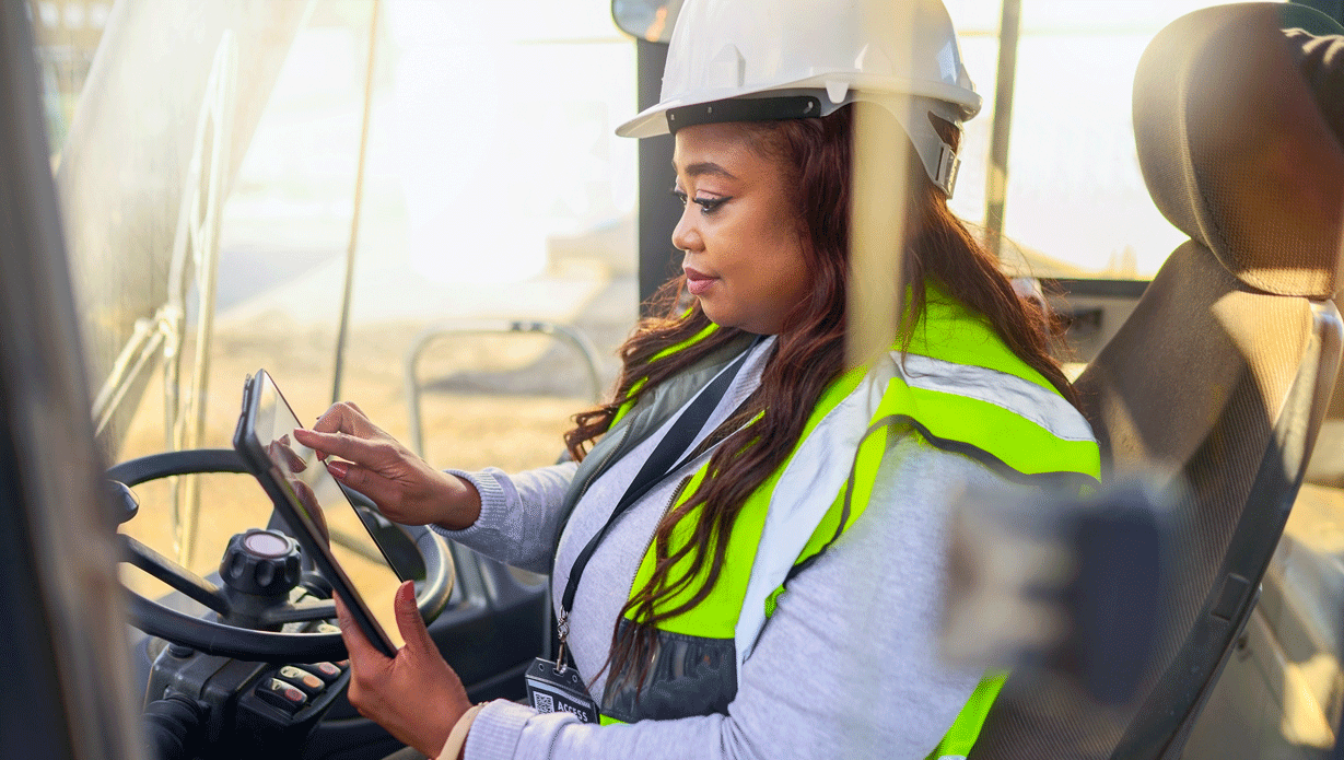 8edaea850cdec975351289f49c55150e (1).png Woman driving a forklift in a white hard hat and safety vest
